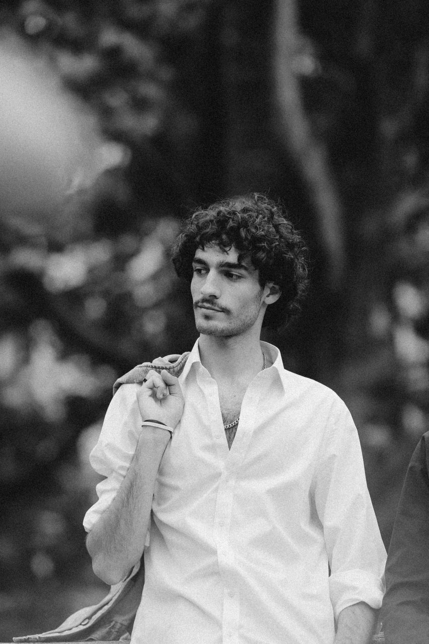 5 Must-Have Wardrobe Essentials for Bangladeshi Men in 2025, Elegant black and white portrait of a man in a white shirt posing outdoors.